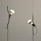 Two Clérachic spotlight pendants with white conical shades hanging on thin cables against a pale block wall.
