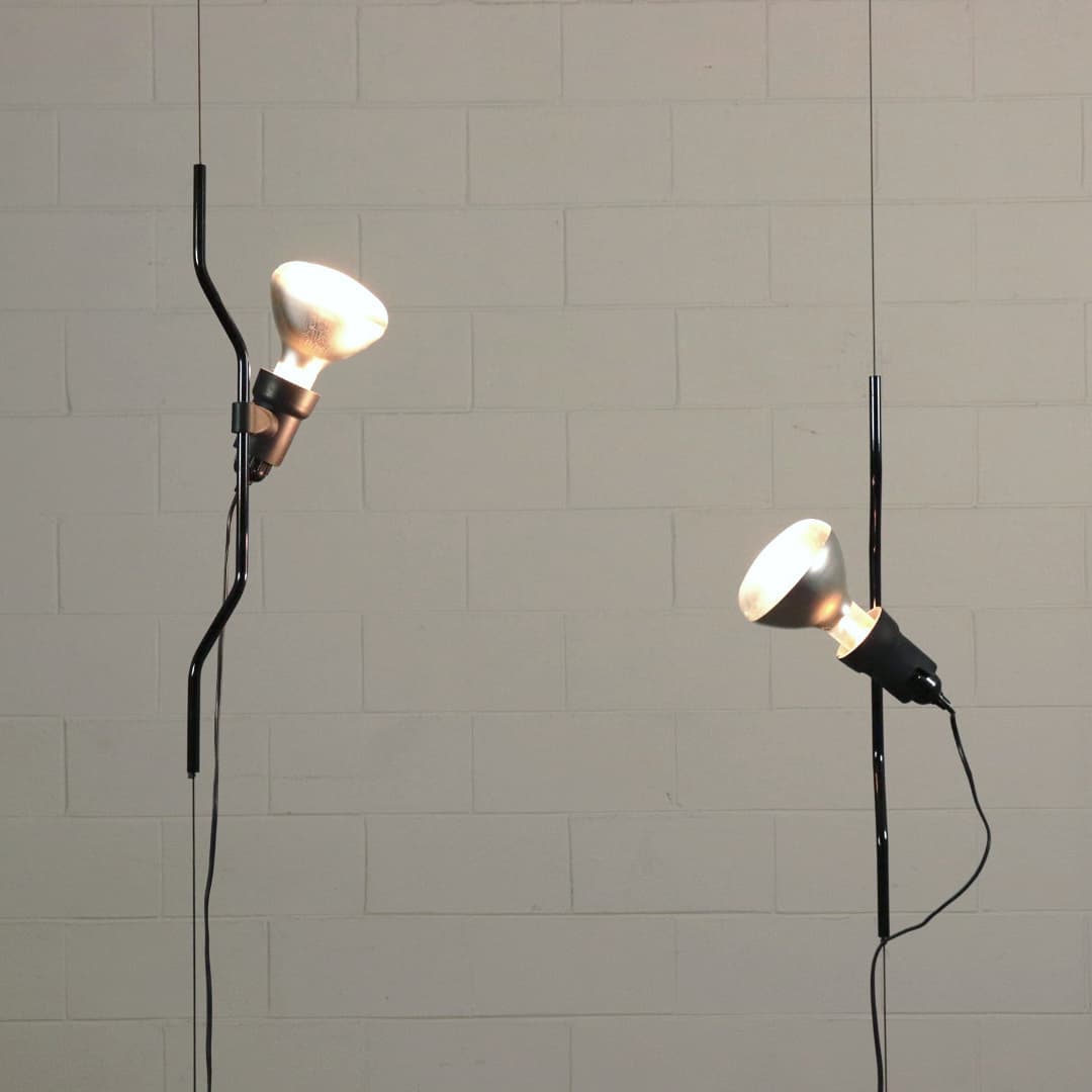Two Clérachic spotlight pendants with white conical shades hanging on thin cables against a pale block wall.
