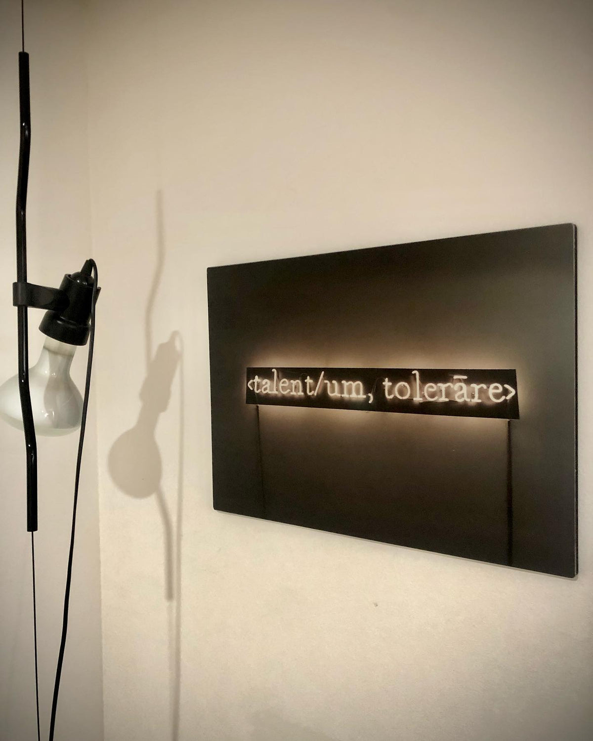 Close view of a Clérachic pendant with a black bendable cord and a white bulb, beside a dark wall sign with softly lit text.
