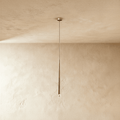 Clérachic single slender gold cone pendant with a clear crystal tip, hanging on a fine cord from a small canopy against limewashed plaster.