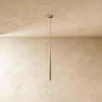 Clérachic single slender gold cone pendant with a clear crystal tip, hanging on a fine cord from a small canopy against limewashed plaster.