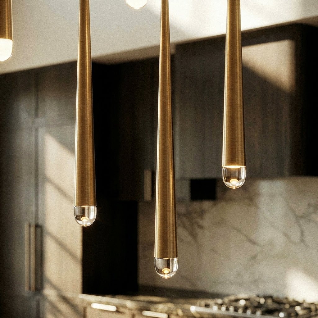 Close view of three Clérachic gold cone pendants with brushed tapered tubes and clear rounded crystal tips lit from within.