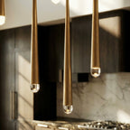 Close view of three Clérachic gold cone pendants with brushed tapered tubes and clear rounded crystal tips lit from within.