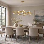 Dining room with a Clérachic chandelier above a long pale table with grey chairs, beside a landscape painting and a window.