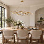 Unlit view of this Clérachic branch chandelier, its white blossoms and gold twigs spanning the room above a wood dining table.