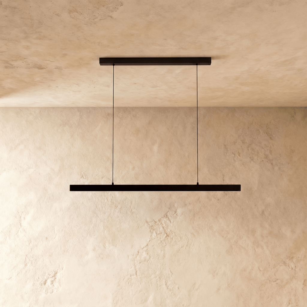 Clérachic black linear pendant light hangs from twin cables against a warm limewash wall and ceiling.