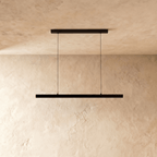 Clérachic black linear pendant light hangs from twin cables against a warm limewash wall and ceiling.