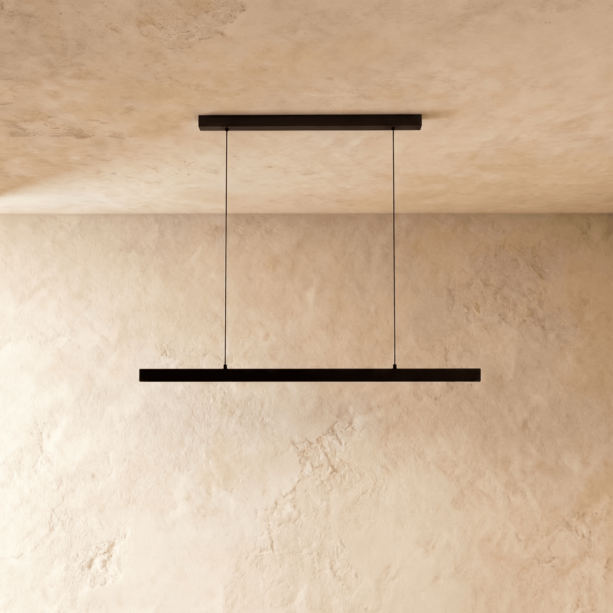 Clérachic black linear pendant light hangs from twin cables against a warm limewash wall and ceiling.