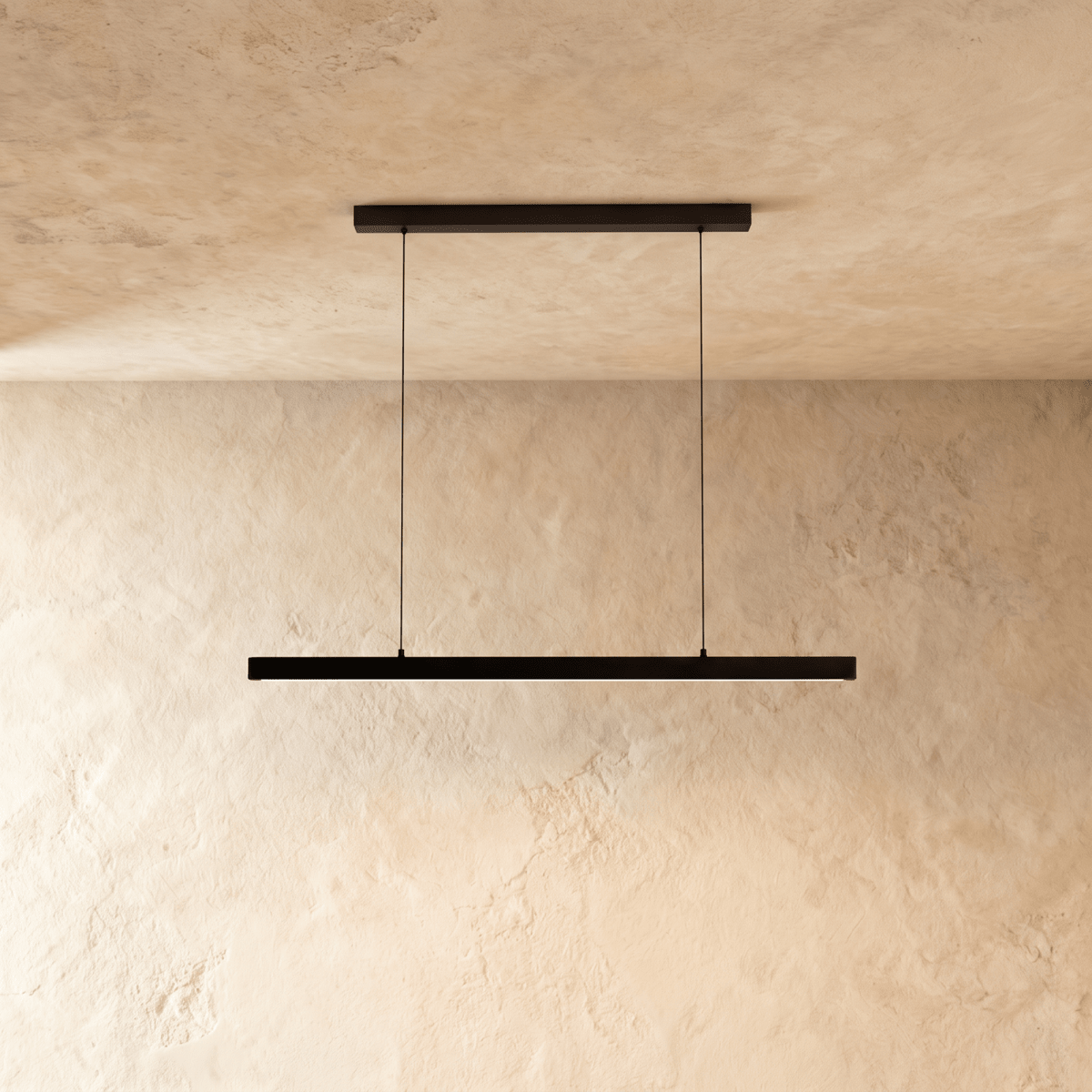 Clérachic black linear pendant, cable-suspended, centred against a textured limewash wall in soft daylight.