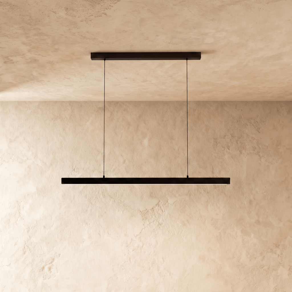 Clérachic black linear pendant bar hangs low from a plaster ceiling, framed by a warm limewash backdrop.
