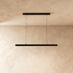 Clérachic black linear pendant bar hangs low from a plaster ceiling, framed by a warm limewash backdrop.