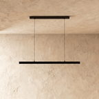 Clérachic black linear pendant light suspended by two thin cables above a sand-toned limewash wall.