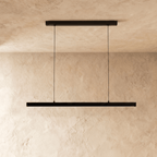 Clérachic black linear pendant light hangs centred, its cables taut, against a warm limewash backdrop.