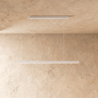 Clérachic white linear pendant bar hangs low from a plaster ceiling, framed by a warm limewash backdrop.