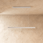 Clérachic white linear pendant light suspended by two thin cables above a sand-toned limewash wall.