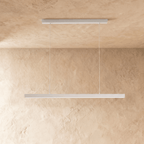 Clérachic white linear pendant, its slim bar catching the light, hangs against a warm plaster wall.