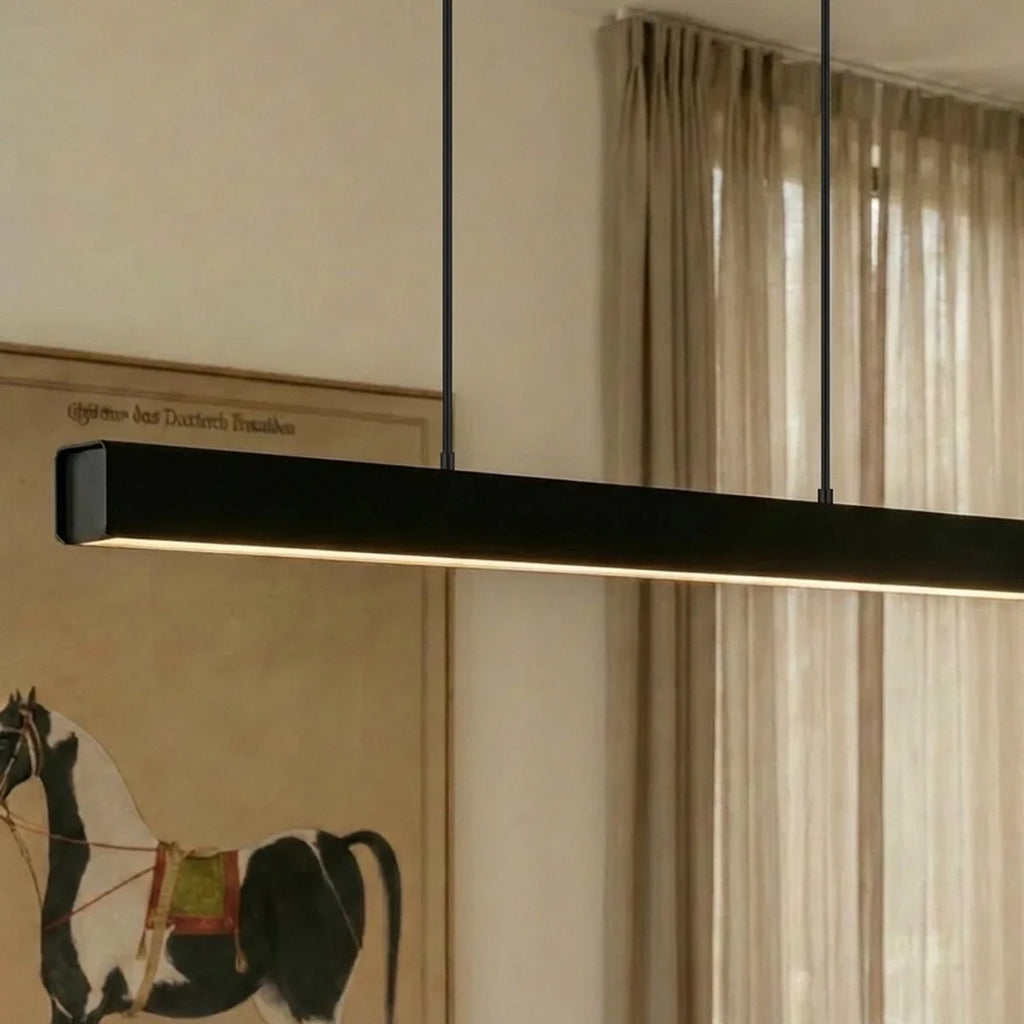Clérachic black linear pendant glows warm above a dining table, its slim bar lit against a framed print.