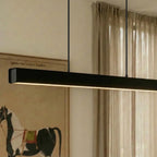 Clérachic black linear pendant glows warm above a dining table, its slim bar lit against a framed print.