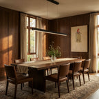 Clérachic black linear pendant lights a long walnut dining table in a wood-panelled room with linen curtains.