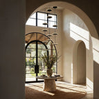 Clérachic staircase chandelier of slim black LED discs on long rods, hung in a tall arched entrance hall above a round table.