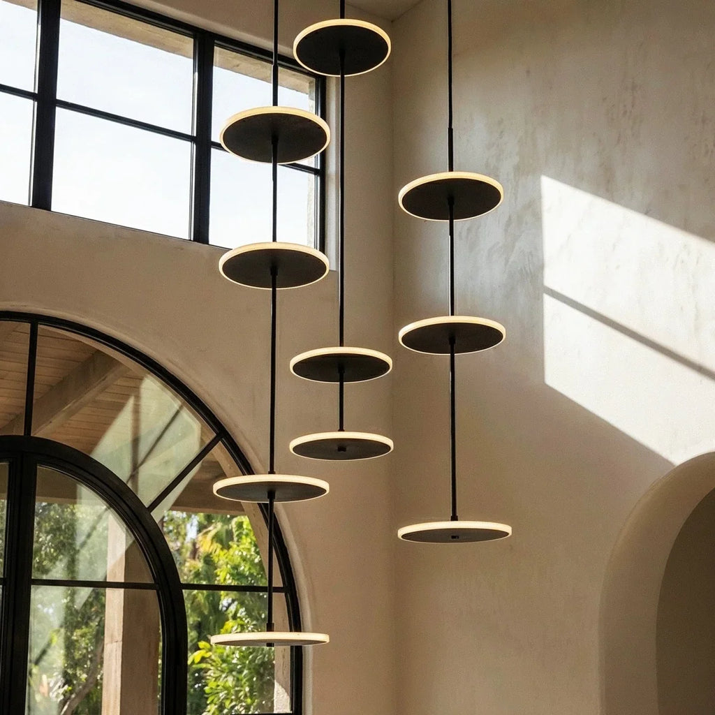 Clérachic black LED disc pendants at three staggered heights on thin rods, glowing softly against a plaster wall and arched window.