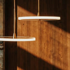 Clérachic close-up of two gold LED discs with frosted edges on brass stems, lit against sunlit wooden panelling.