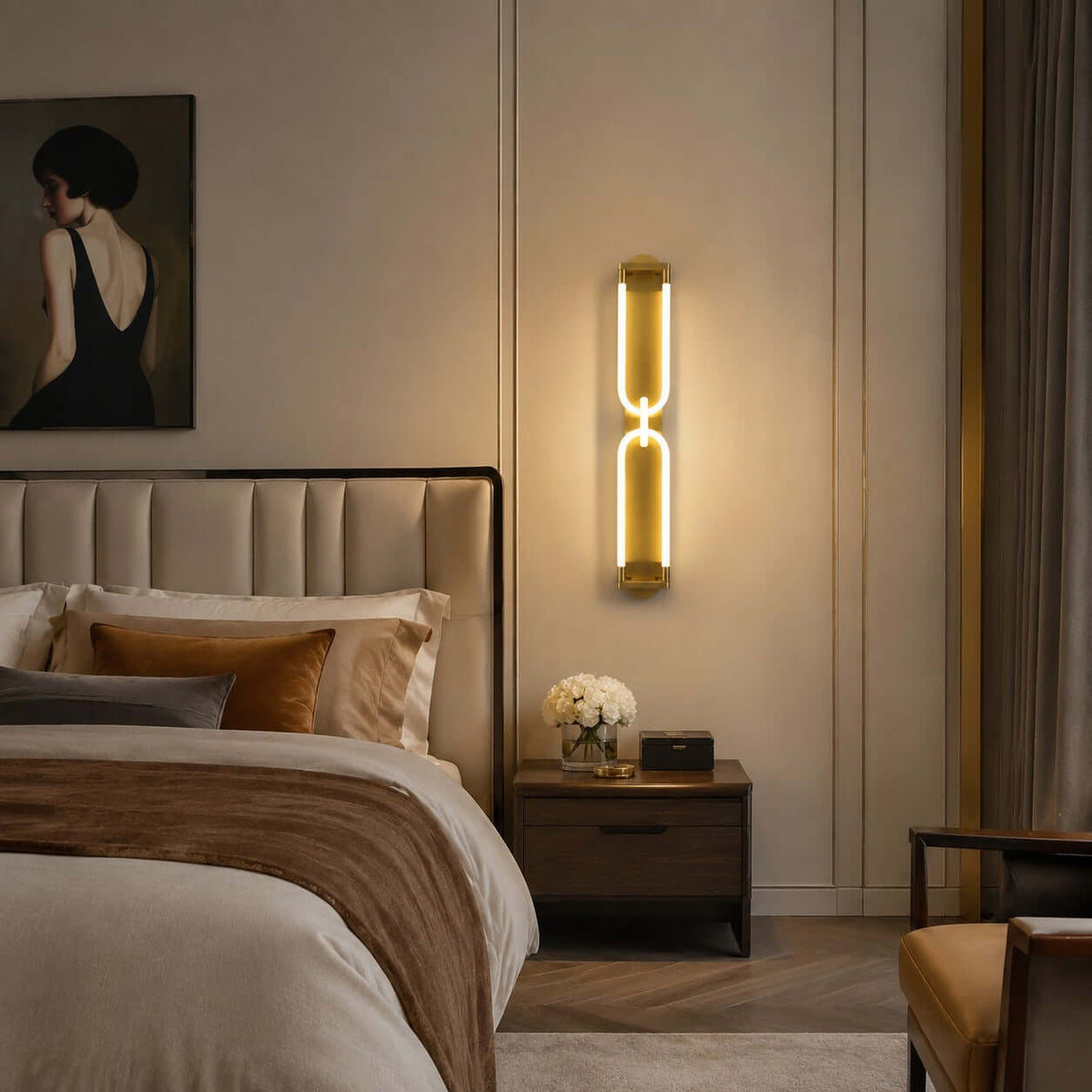 Glowing gold Clérachic wall light on a cream panelled wall above a bedside table, with a framed portrait and a tufted headboard.