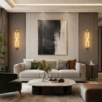 Pair of gold Clérachic wall lights on a taupe panelled wall, either side of a black and cream painting above a white sofa.