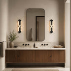 Two black Clérachic wall lights lit either side of a rounded mirror, above a floating walnut vanity with black taps.