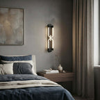 Black Clérachic loop wall light on a grey wall above a bed in navy linen, with a framed textured artwork beside it.