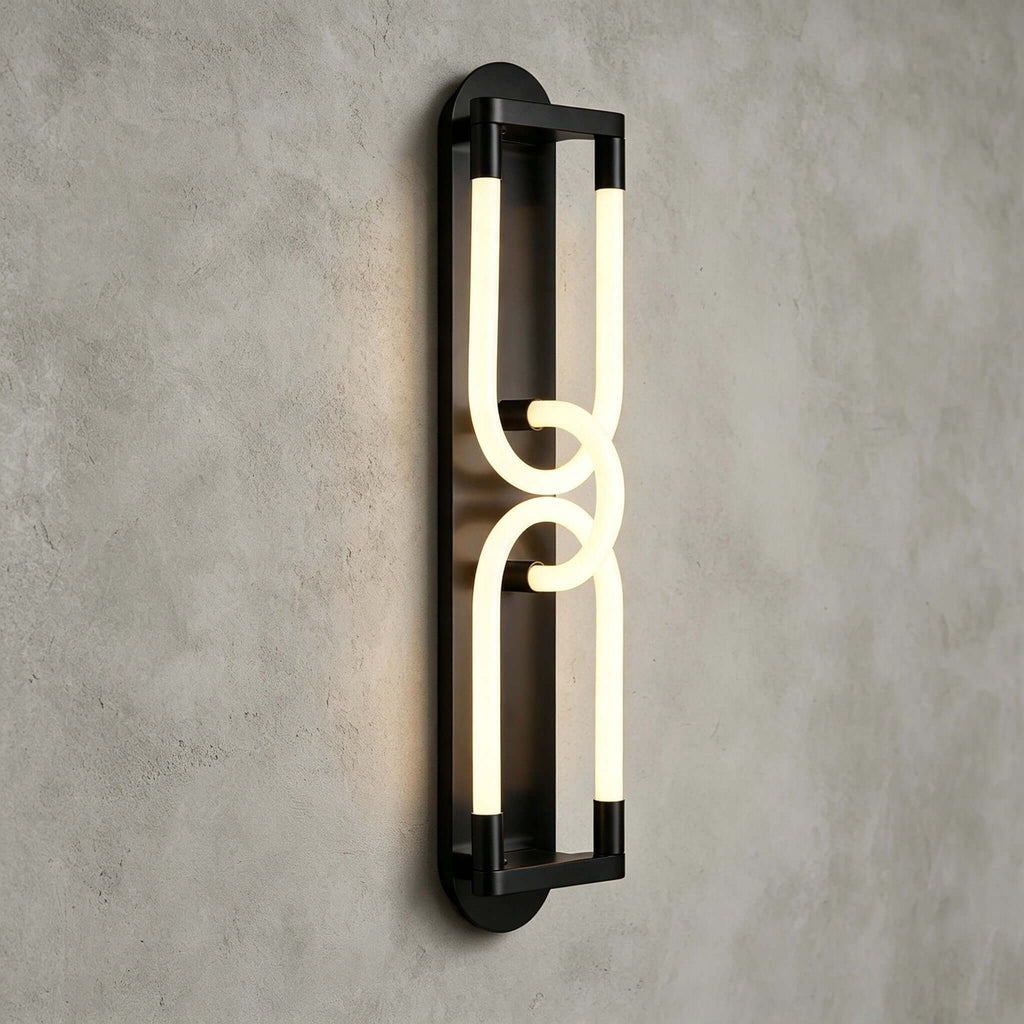 Close view of a lit black Clérachic wall light, two linked frosted loops on a slim frame against grey plaster.
