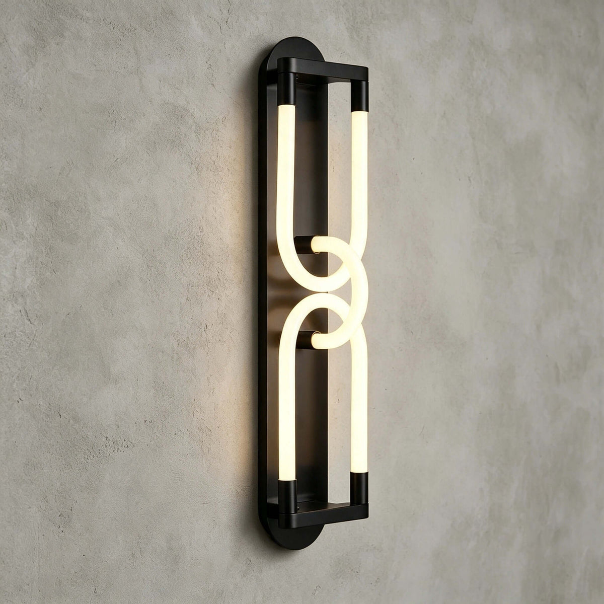 Close view of a lit black Clérachic wall light, two linked frosted loops on a slim frame against grey plaster.