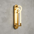 A gold Clérachic loop wall light seen from an angle, the frosted tube glowing warm in front of a brushed brass backplate.