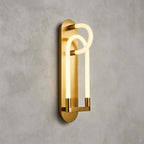 A gold Clérachic loop wall light seen from an angle, the frosted tube glowing warm in front of a brushed brass backplate.