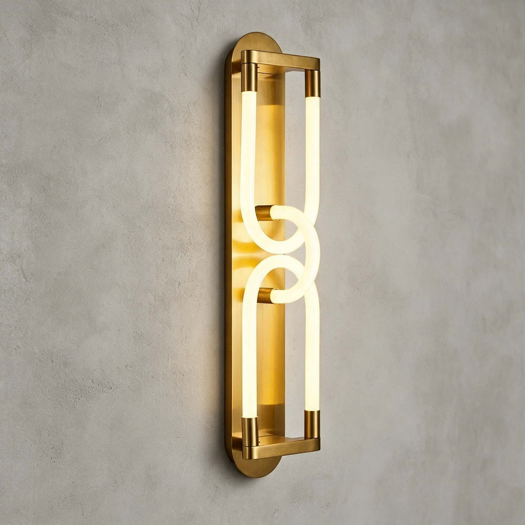 Front view of the lit gold Clérachic wall light, two interlocked loops of light in a brass frame on a grey plaster wall.
