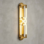 Front view of the lit gold Clérachic wall light, two interlocked loops of light in a brass frame on a grey plaster wall.
