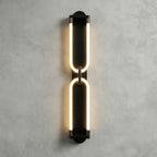 Black Clérachic wall light on a grey plaster wall, two stacked glowing loops joined at the middle by a small link.