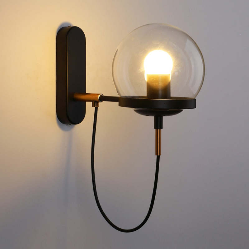 The Clérachic glass globe wall sconce in matte black, lit warm white, with its signature looped cord beneath the globe.