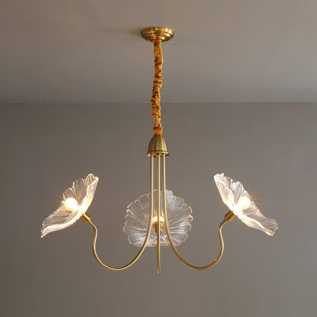 Clear glass version of the Clérachic Lotus Blossom Chandelier, 3-light, its ruffled shades lit against a grey wall.