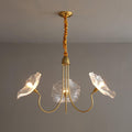 Clear glass version of the Clérachic Lotus Blossom Chandelier, 3-light, its ruffled shades lit against a grey wall.