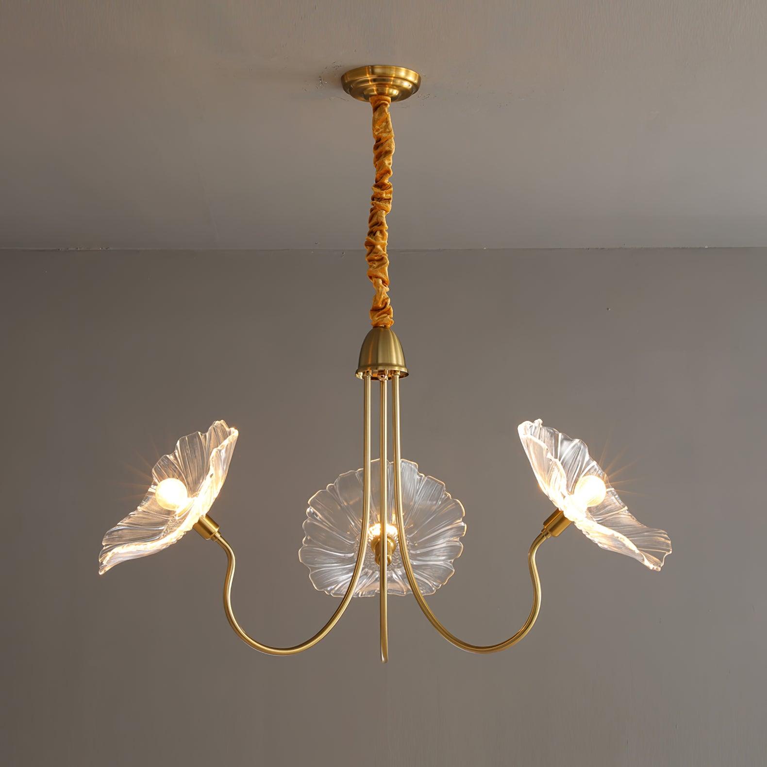 Clear glass version of the Clérachic Lotus Blossom Chandelier, 3-light, its ruffled shades lit against a grey wall.