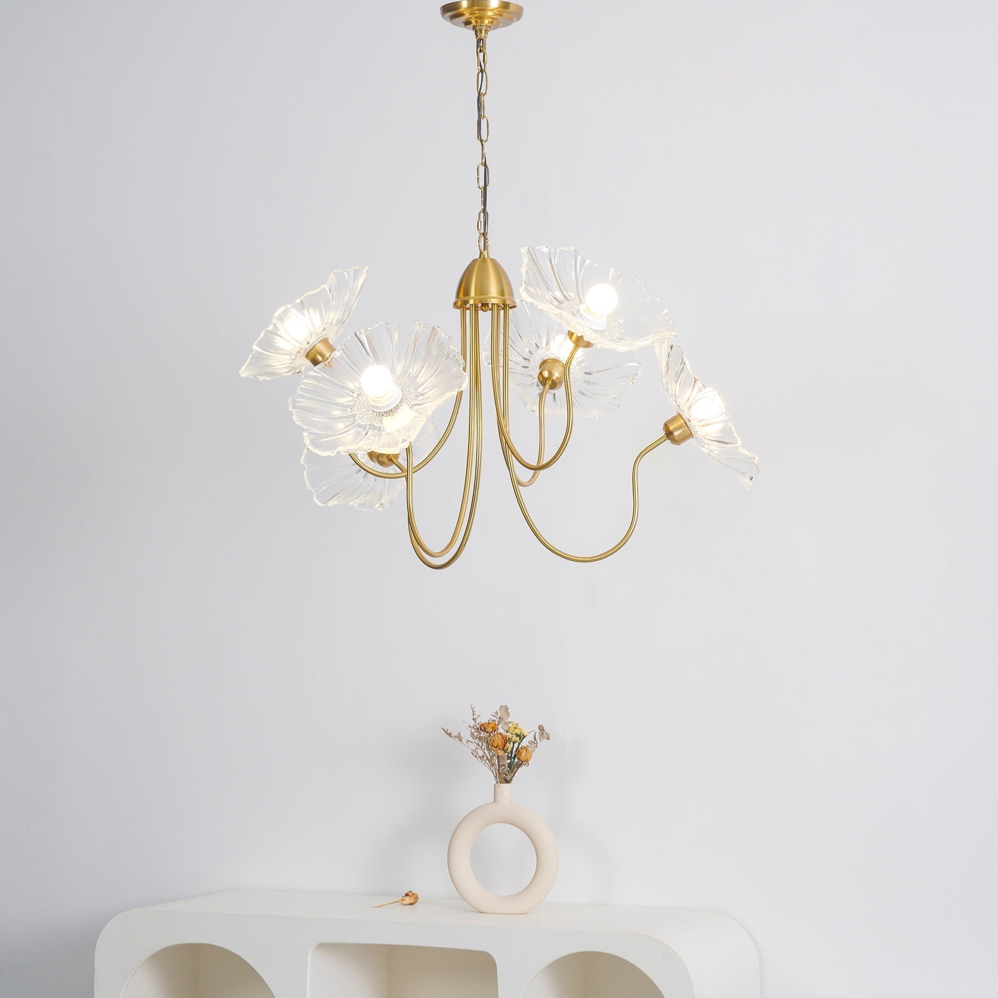Clear glass shades of the Clérachic Lotus Blossom Chandelier lit above a pale console styled with dried flowers.