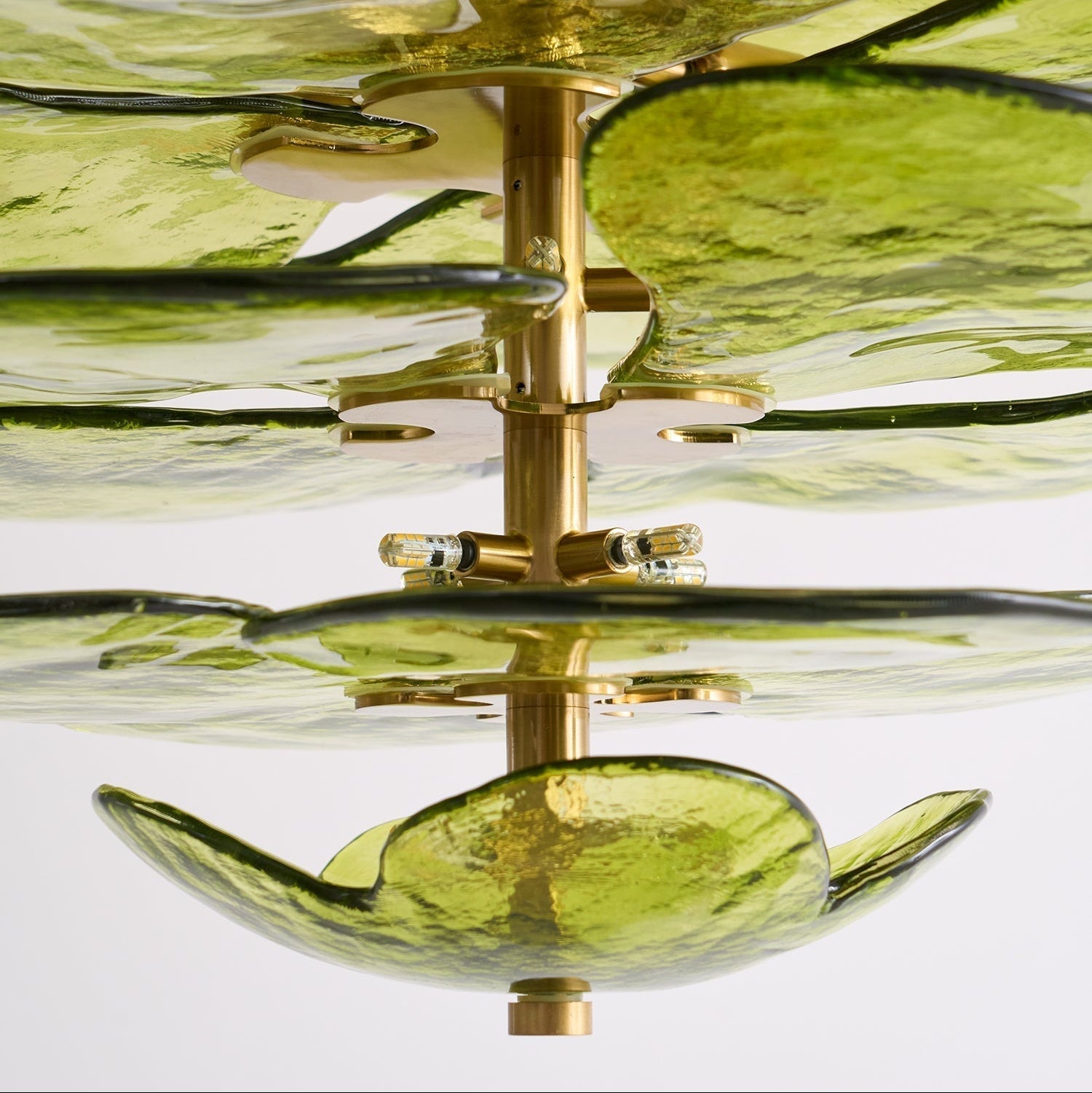 Close-up of the Clérachic chandelier's brass column, disc mounts and capsule bulbs between the green glass leaves.