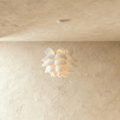 Clérachic white petal-layered pendant glowing warm on a slim white cord and canopy, against a limewashed wall.