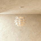 Clérachic white petal-layered pendant glowing warm on a slim white cord and canopy, against a limewashed wall.
