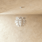 Clérachic white petal-layered pendant, unlit, hung from a thin white cord and round canopy on a plaster wall.