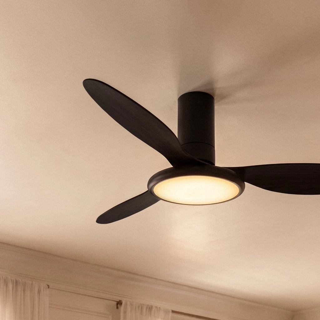 Close up of the Clérachic matte black ceiling fan with a light, showing dark blades and a glowing round LED disc.
