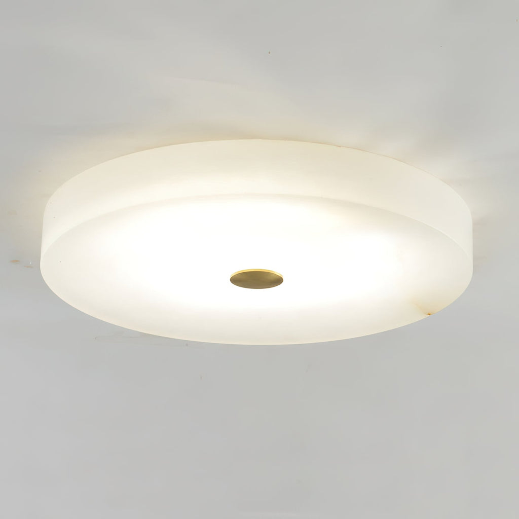 Clérachic drum flush mount ceiling light lit against a plain ceiling, the alabaster glowing honey around its brass centre cap.