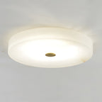 Clérachic drum flush mount ceiling light lit against a plain ceiling, the alabaster glowing honey around its brass centre cap.