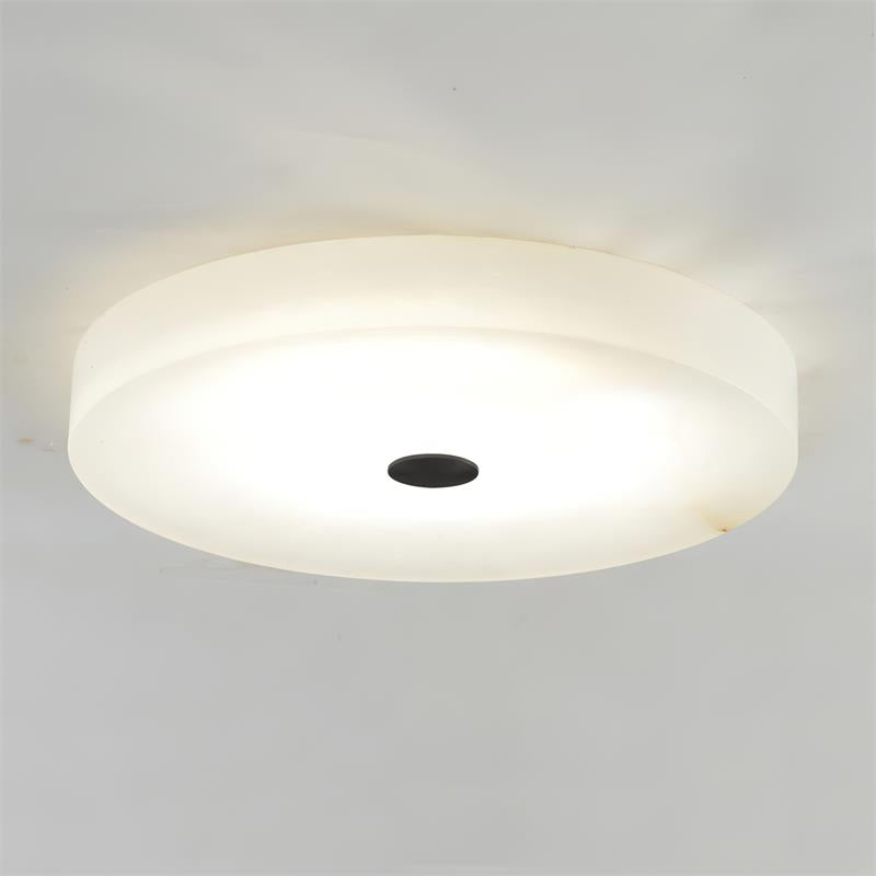 Lit close-up of the Clérachic flush mount ceiling light with the matte black cap, alabaster warming to cream across its underside.